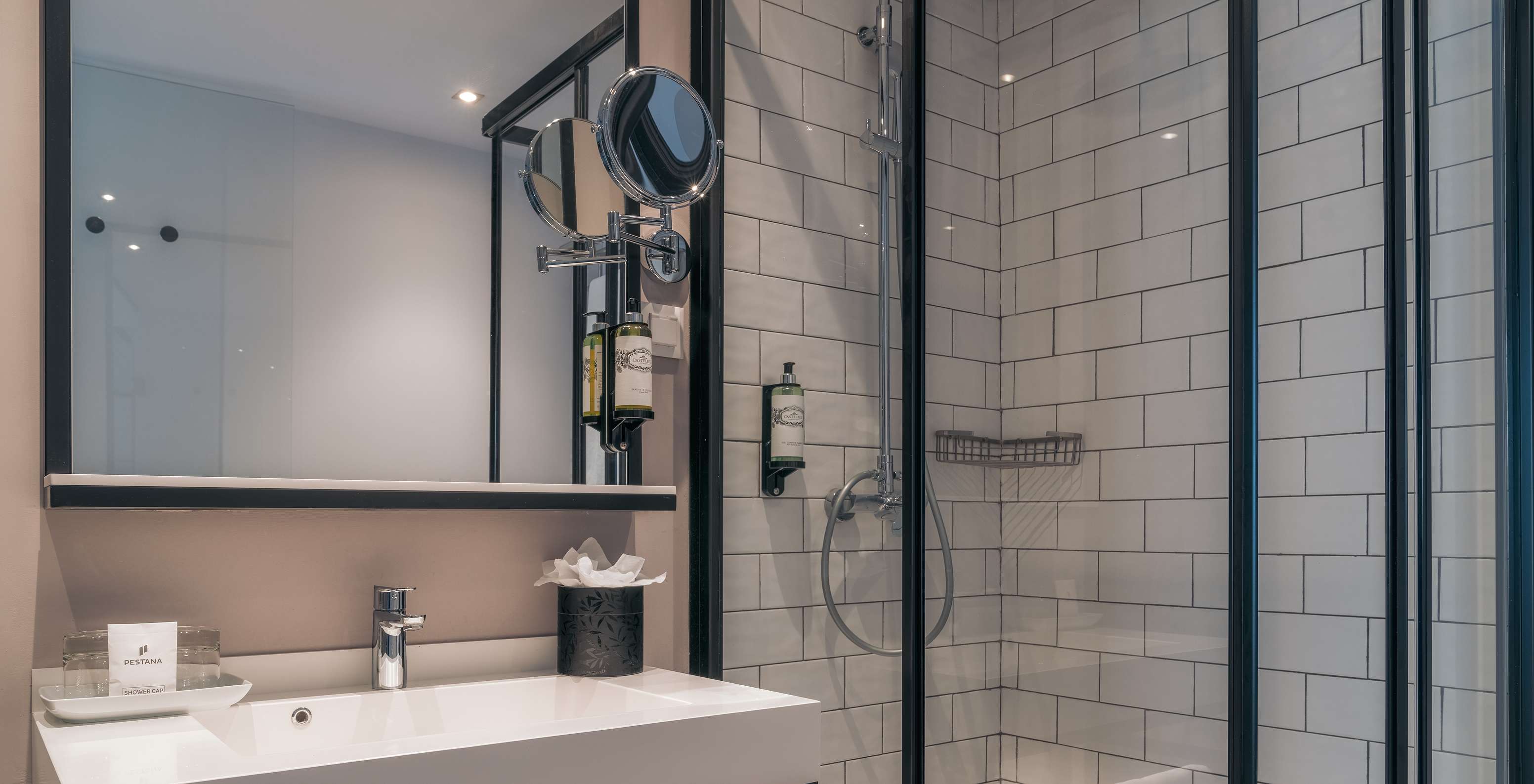 O Vintage do Pestana Lisboa Vintage tem um duche com portas de vidro e detalhes pretos e um lavatório com dois espelhos