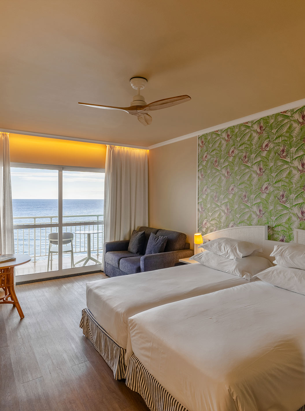 O Premium Sea View do Pestana Ocean Bay All Inclusive tem uma cama dupla, papel de parede com palmeiras, um sofá e varanda