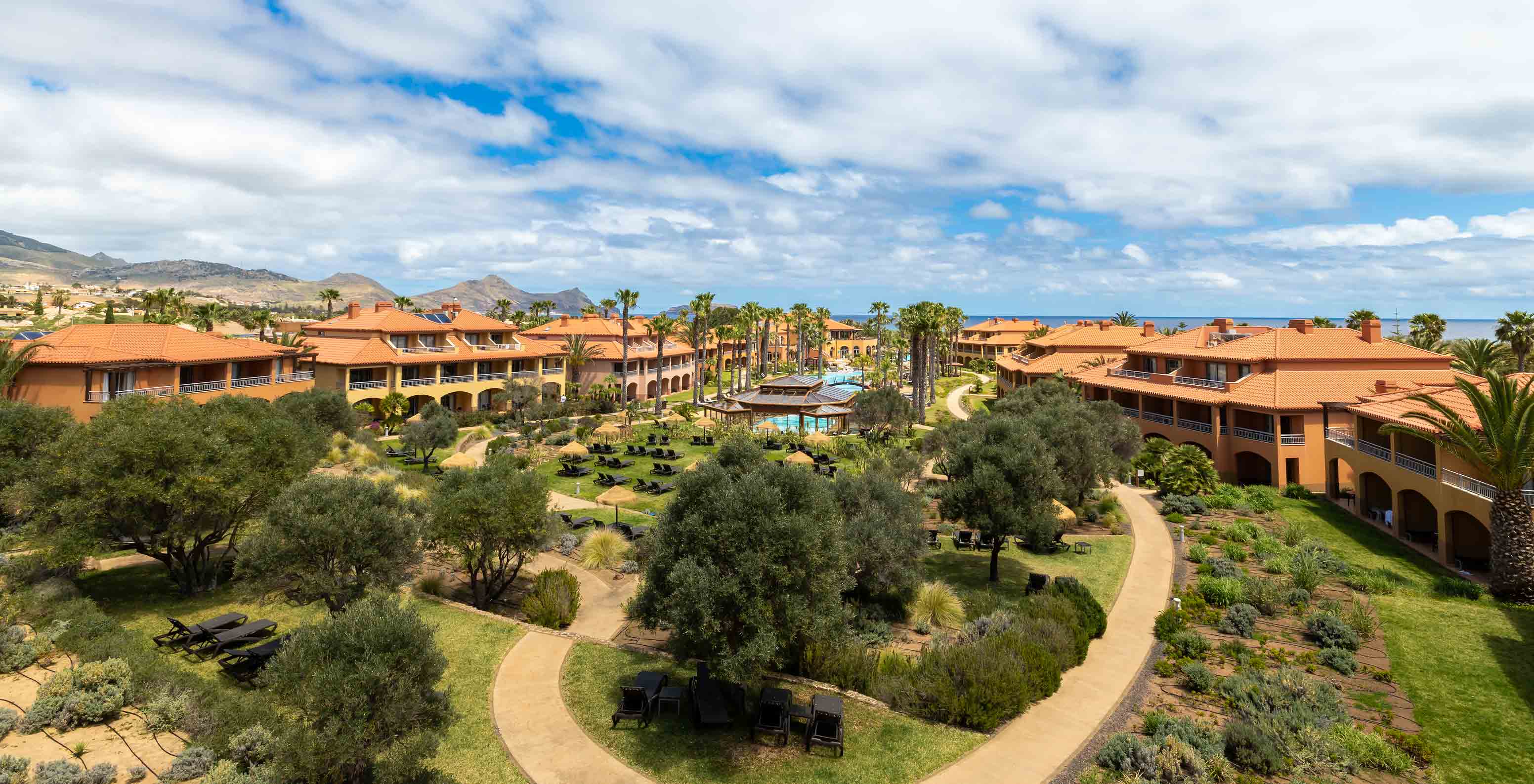 Jardins do Pestana Porto Santo All Inclsuive com relva, palmeiras tropicais, espreguiçadeiras e vilas em redor