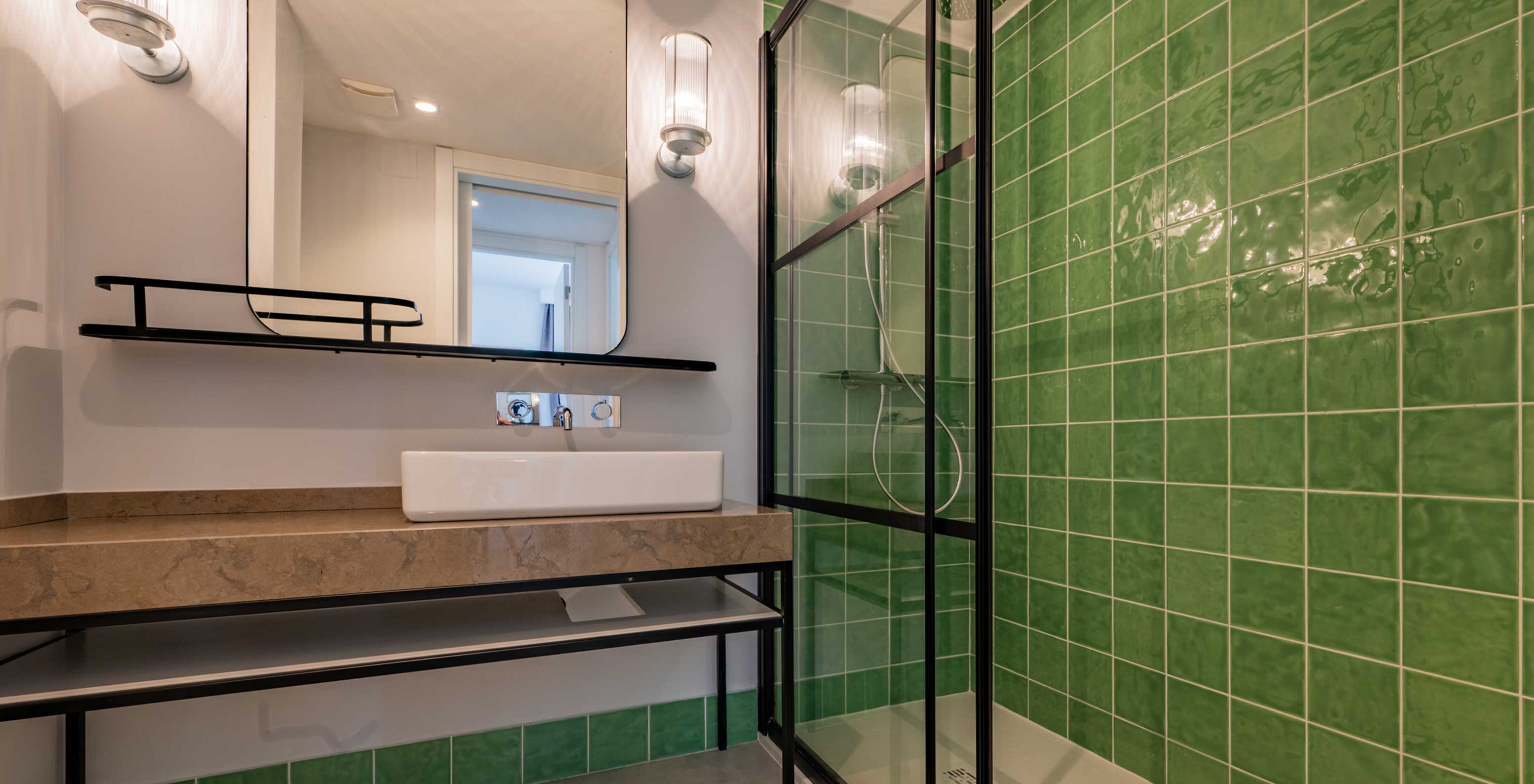 Casa de banho com lavatório branco, espelho grande e duche com azulejos verdes no Pestana Porto Covo Village