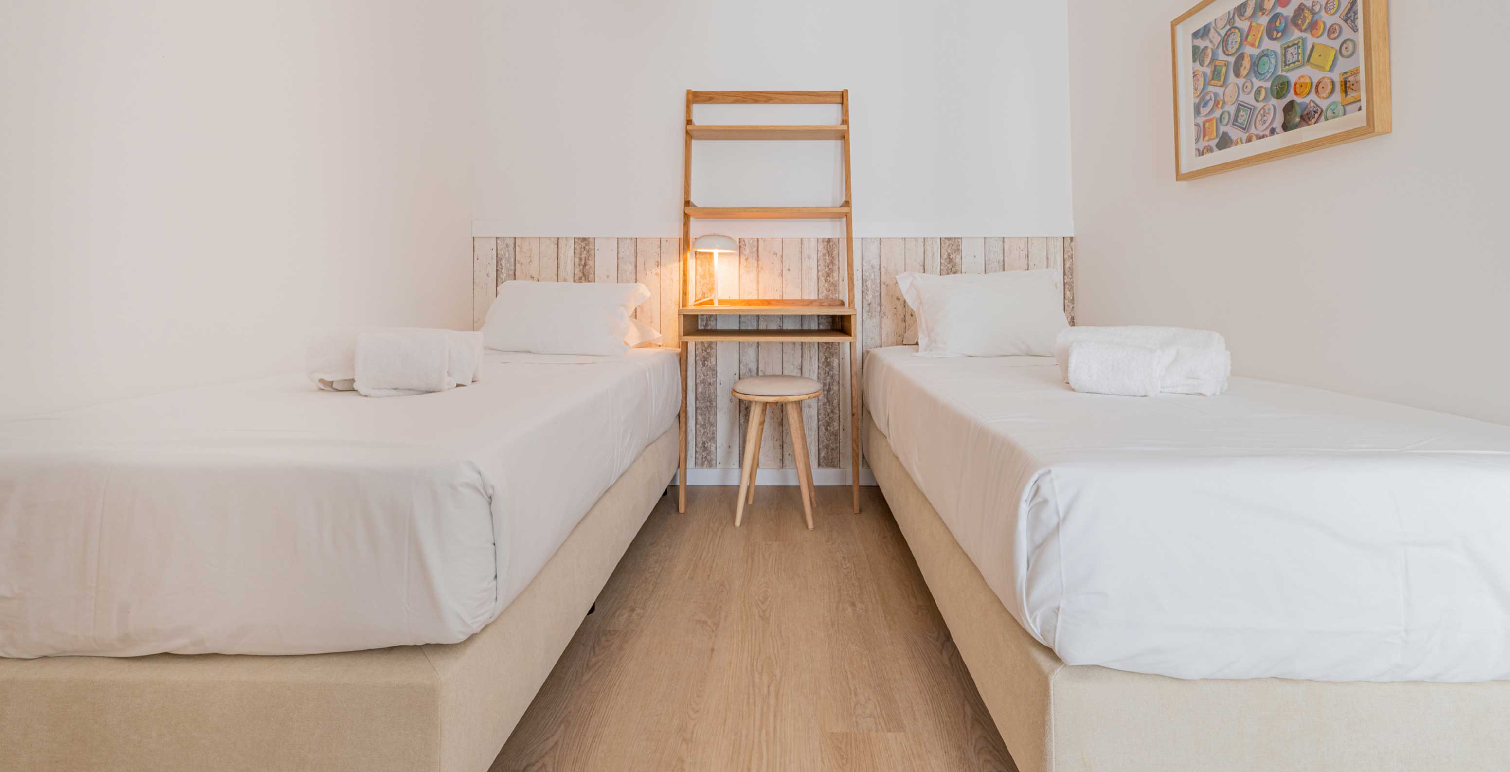 Quarto com duas camas individuais, mesa de madeira com candeeiro e quadro colorido na parede no Pestana Porto Covo Village