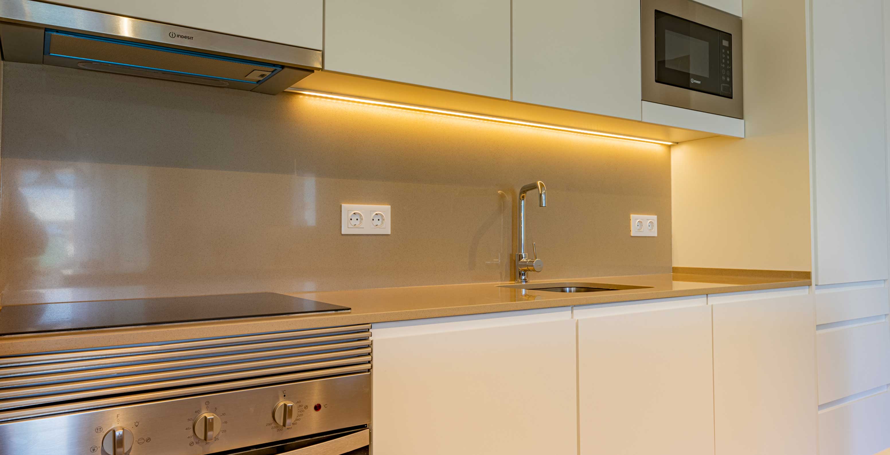 Cozinha moderna do Pestana Porto Covo Village com bancada bege, forno embutido, micro-ondas e iluminação sob armários