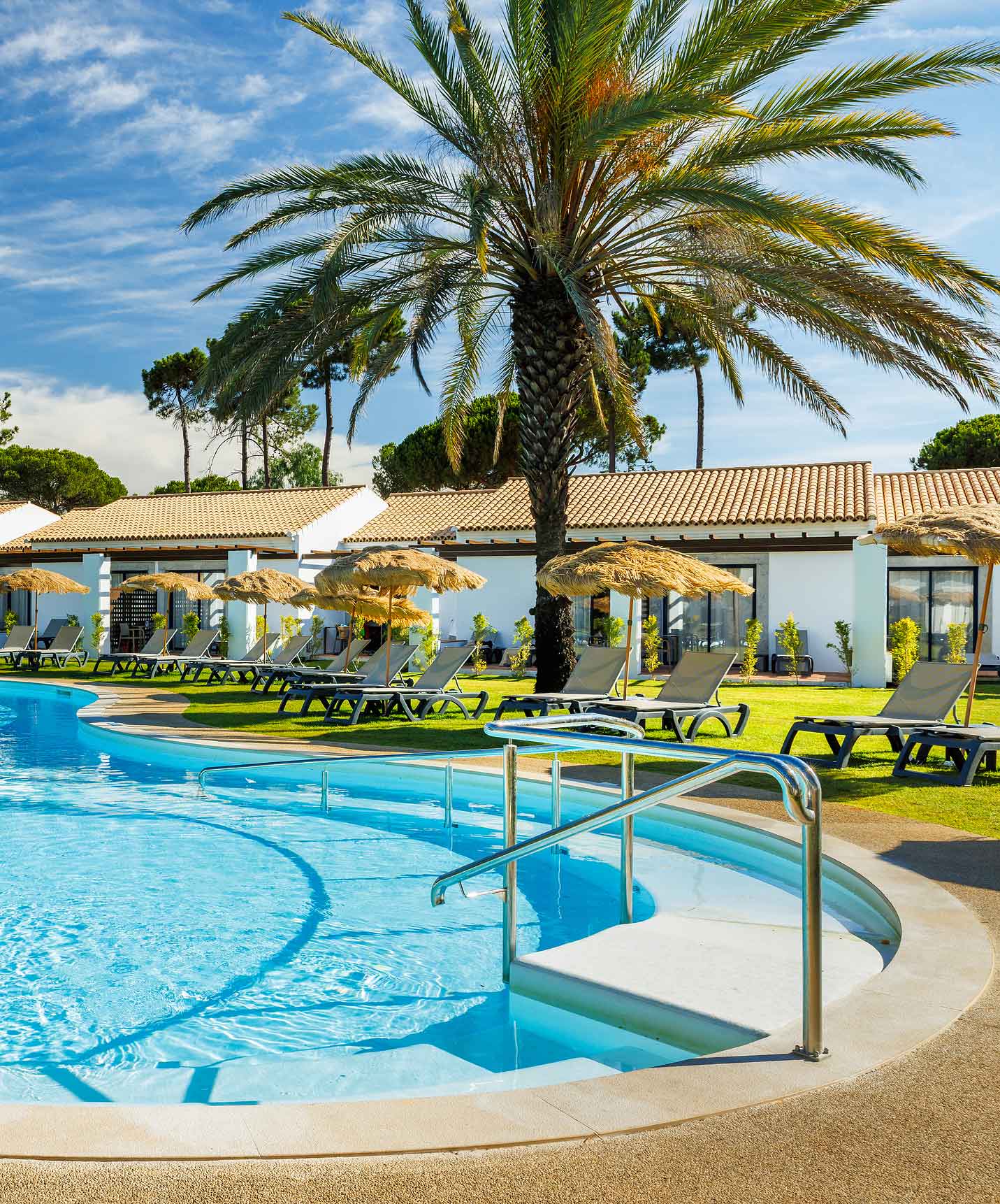 Pestana Vila Sol, Hotel com Golfe e Spa no Algarve, com uma piscina exterior rodeada por espreguiçadeiras, palmeiras e guarda-sóis de palha sob um céu azul