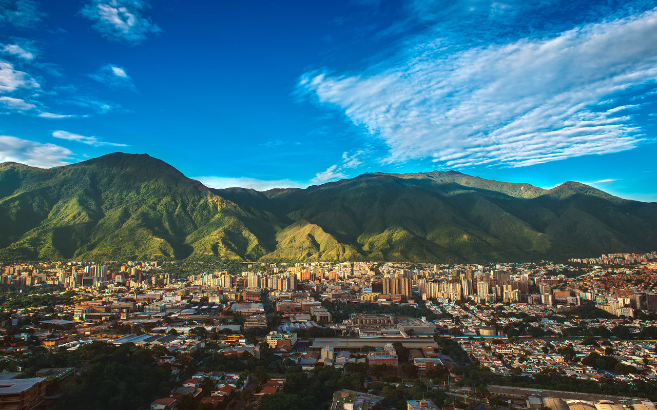 Luchtfoto van de stad Caracas met hoge gebouwen, in contrast met de bergachtige natuur en de blauwe lucht