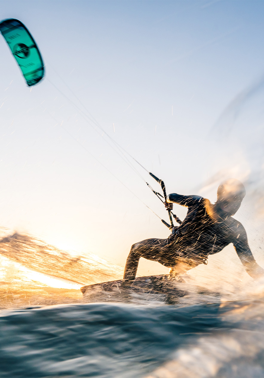 Man kitesurfing in the sea with a blue sail and water splashing with the sun reflecting on the water