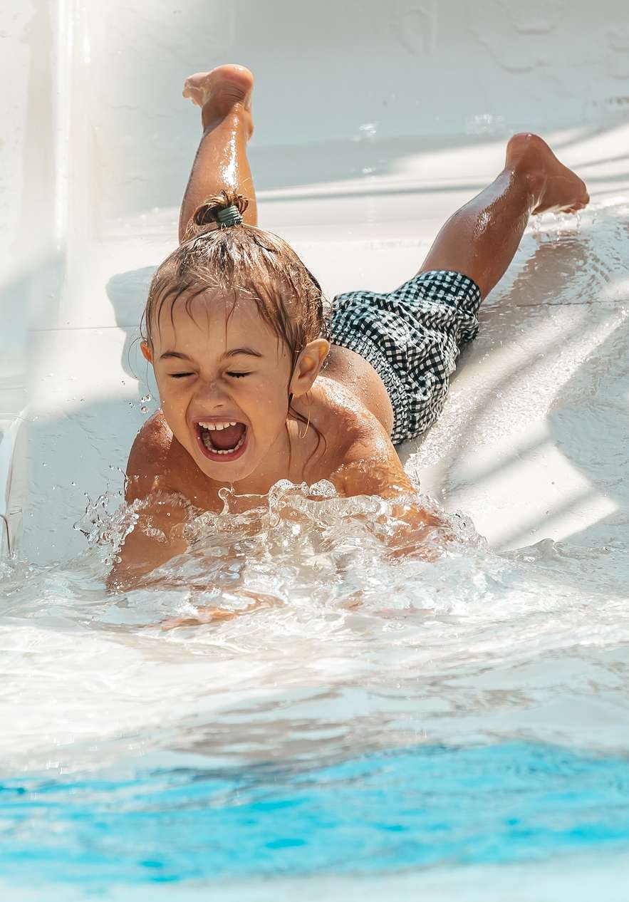 Smiling child sliding down the slide at Slide & Splash park towards the pool