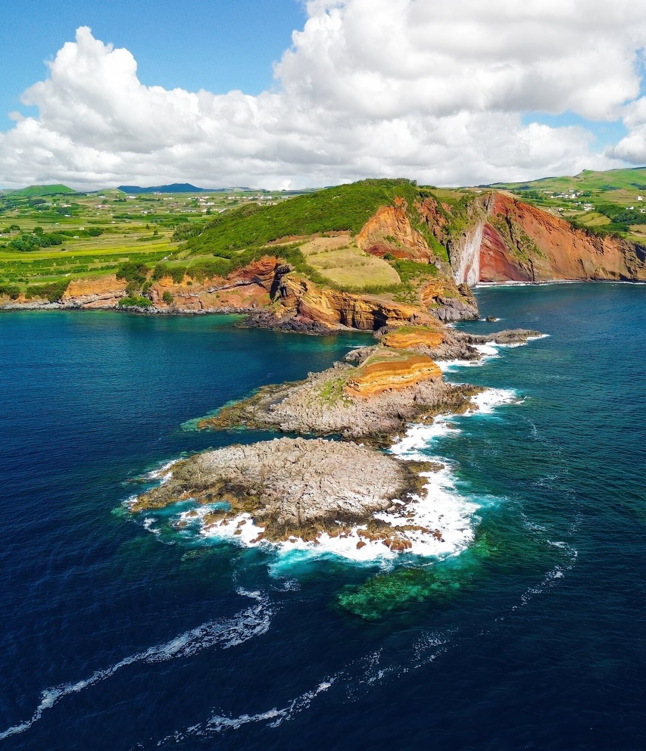 Aerial view of volcanic rock formations sculpted by the sea, surrounded by the ocean and green vegetation