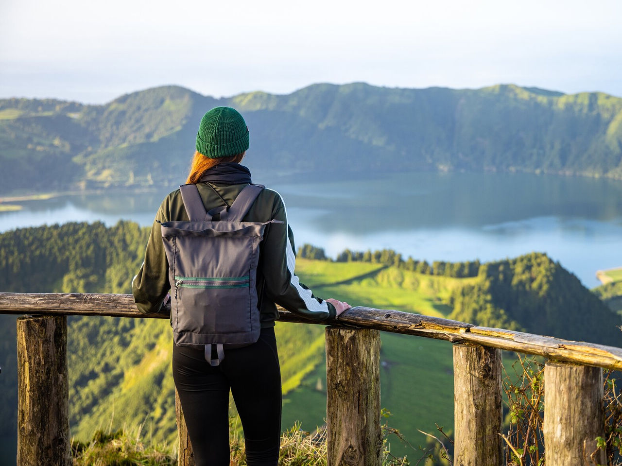 Person walking on a green trail, admiring the serene view of a blue lagoon surrounded by hills and vegetation