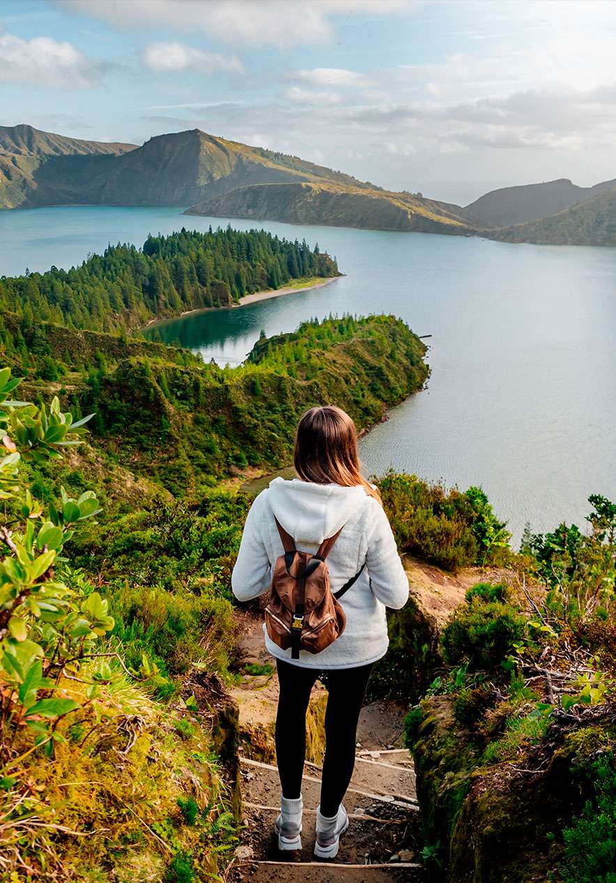 Girl with a backpack climbs the stairs leading to the magnificent Lagoa do Fogo surrounded by nature