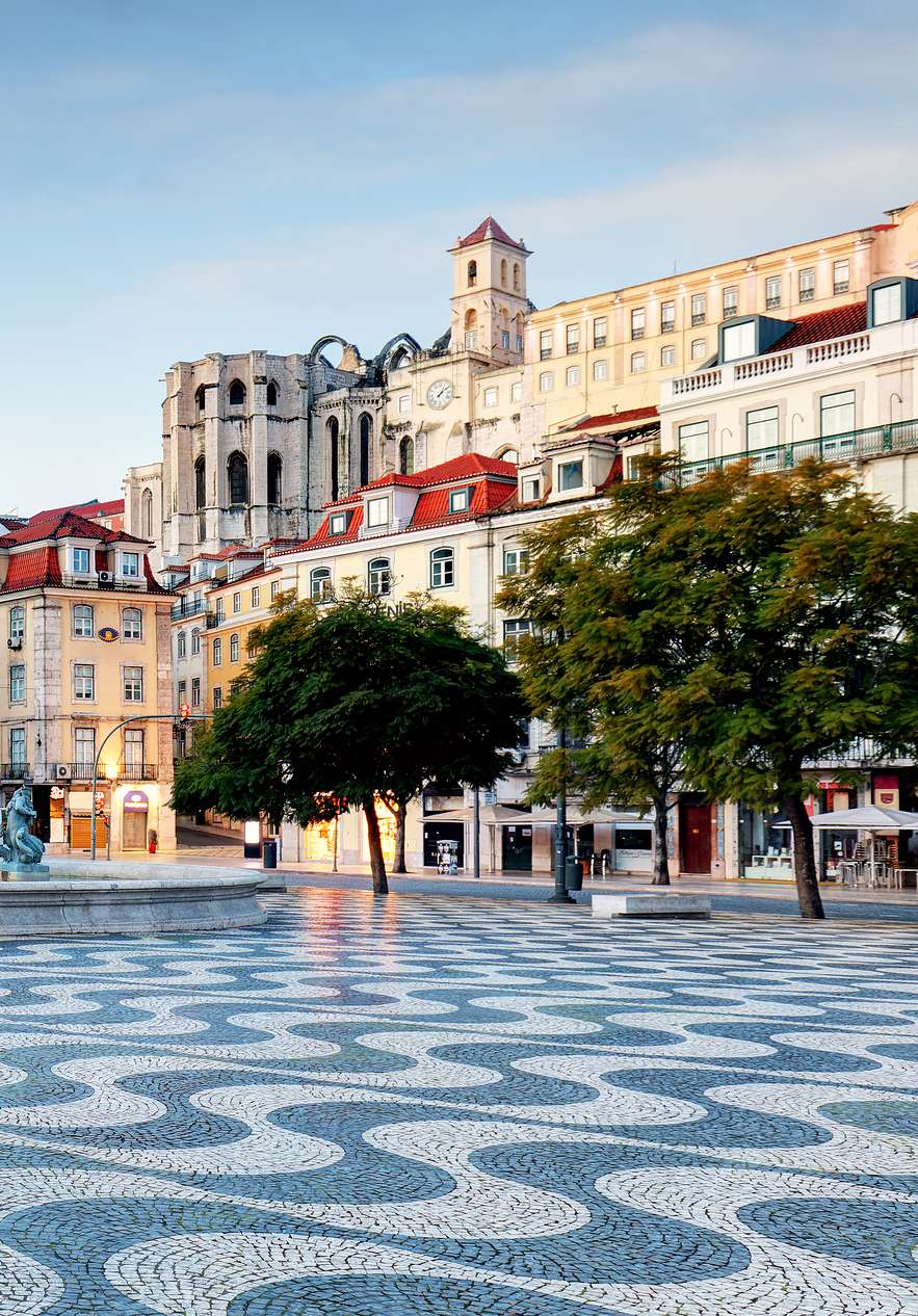 View of Rossio Square with Portuguese pavement a central fountain with statues and several buildings around